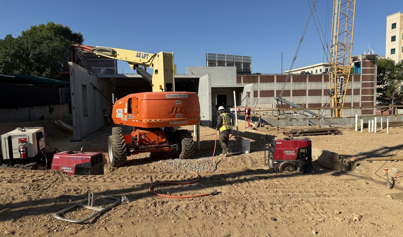 Construction underway at Trinity Central Flats in downtown Atlanta, with a lift and a tower crane working beside the concrete frame of the building's lower floors.